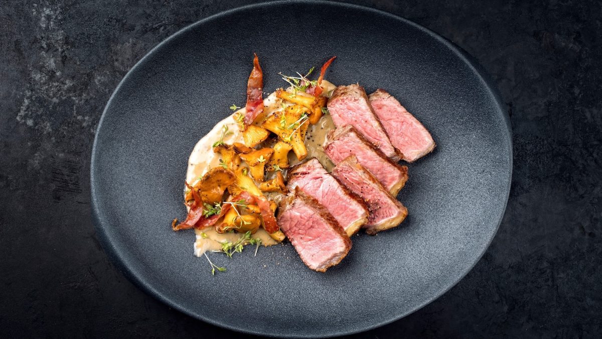 Ein in Scheiben geschnittenes Steak auf einem schwarzen Teller mit Sauce und den Pfifferlingen auf der linken Seite des Tellers.