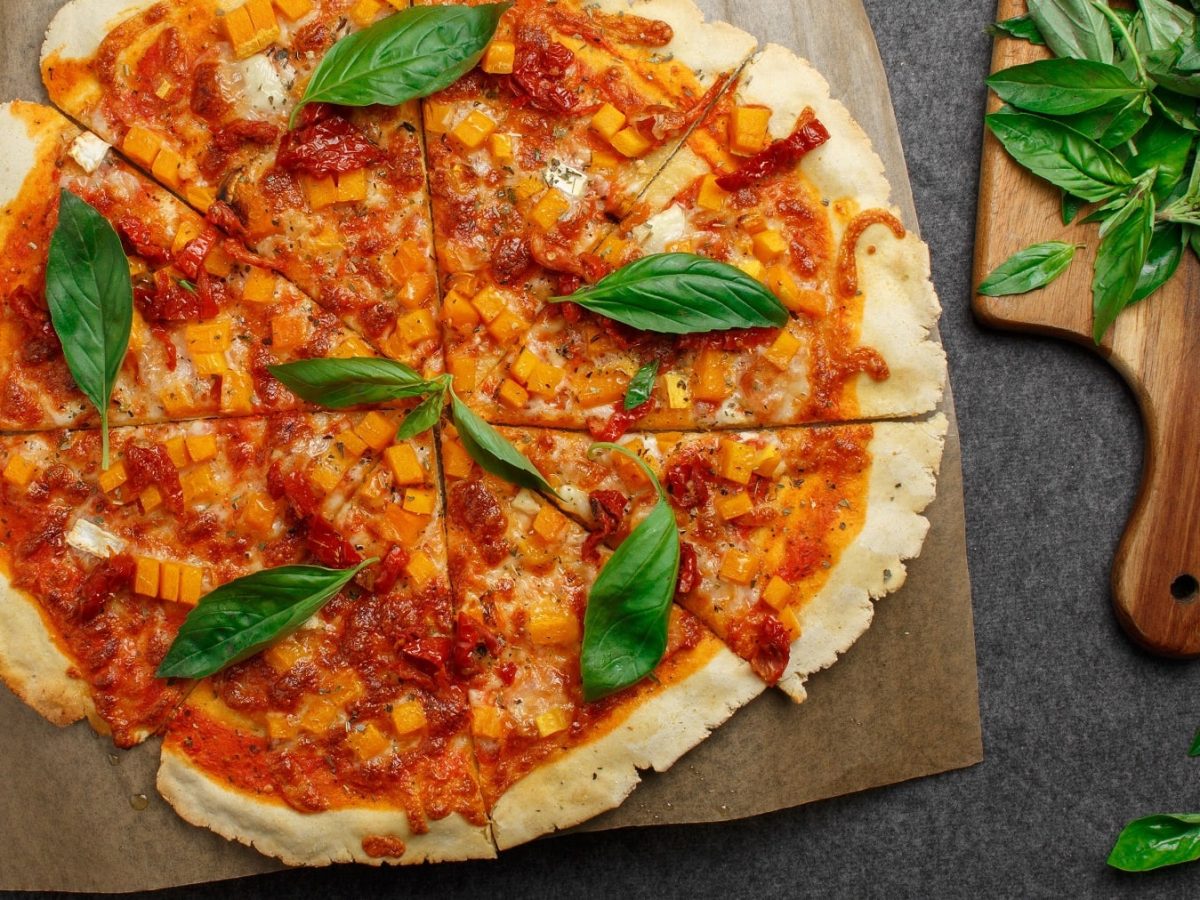 Eine geschnittene Quinoa-Pizzamit Kürbis und Basilikum i der Draufsicht.