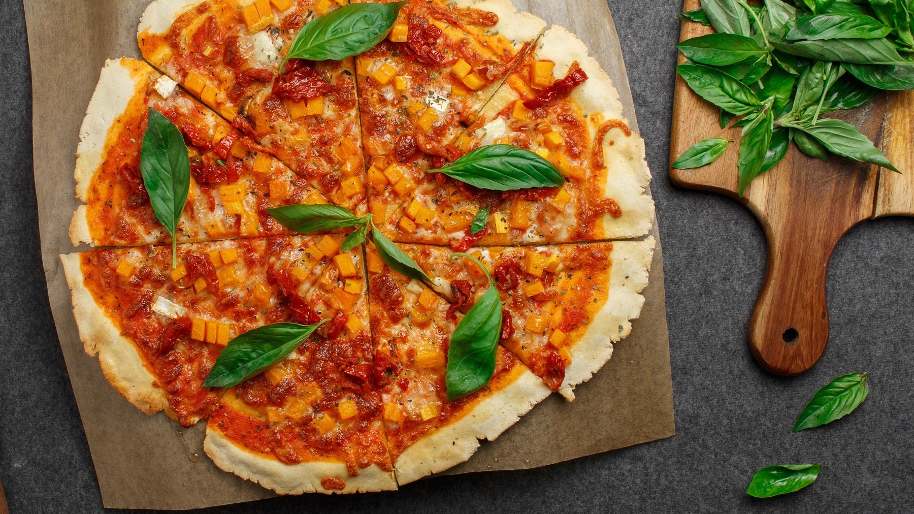 Eine geschnittene Quinoa-Pizzamit Kürbis und Basilikum i der Draufsicht.