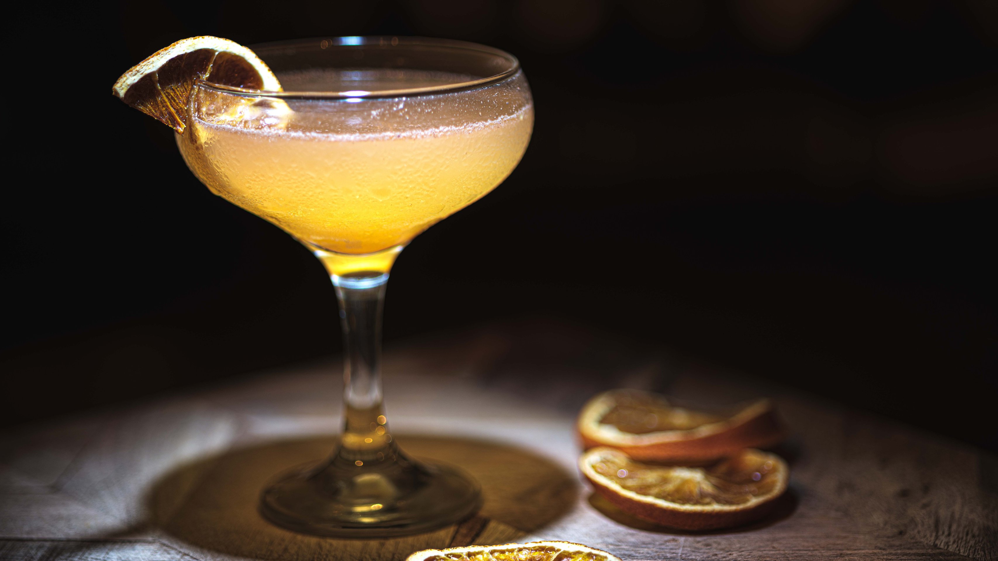 Ein Glas mit dem gelblichen Cocktail auf einem dunklen Holztisch..