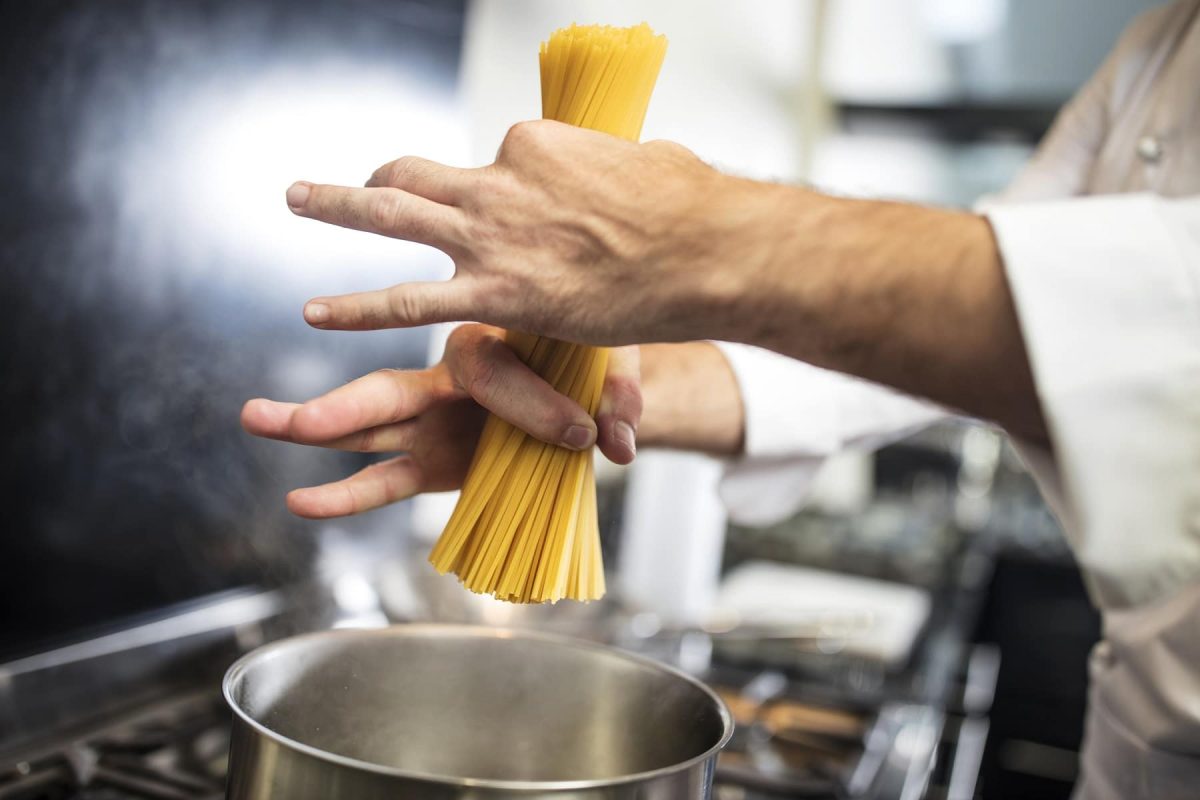Wie viel Pasta pro Person: ein Mann ich Koch-Outfit gibt Spaghetti in einen Topf.