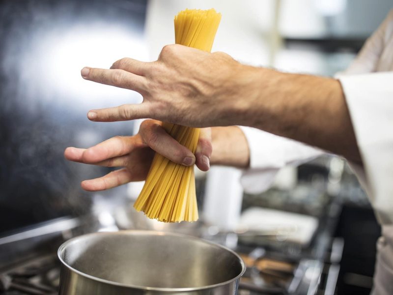 Wie viel Pasta pro Person: ein Mann ich Koch-Outfit gibt Spaghetti in einen Topf.