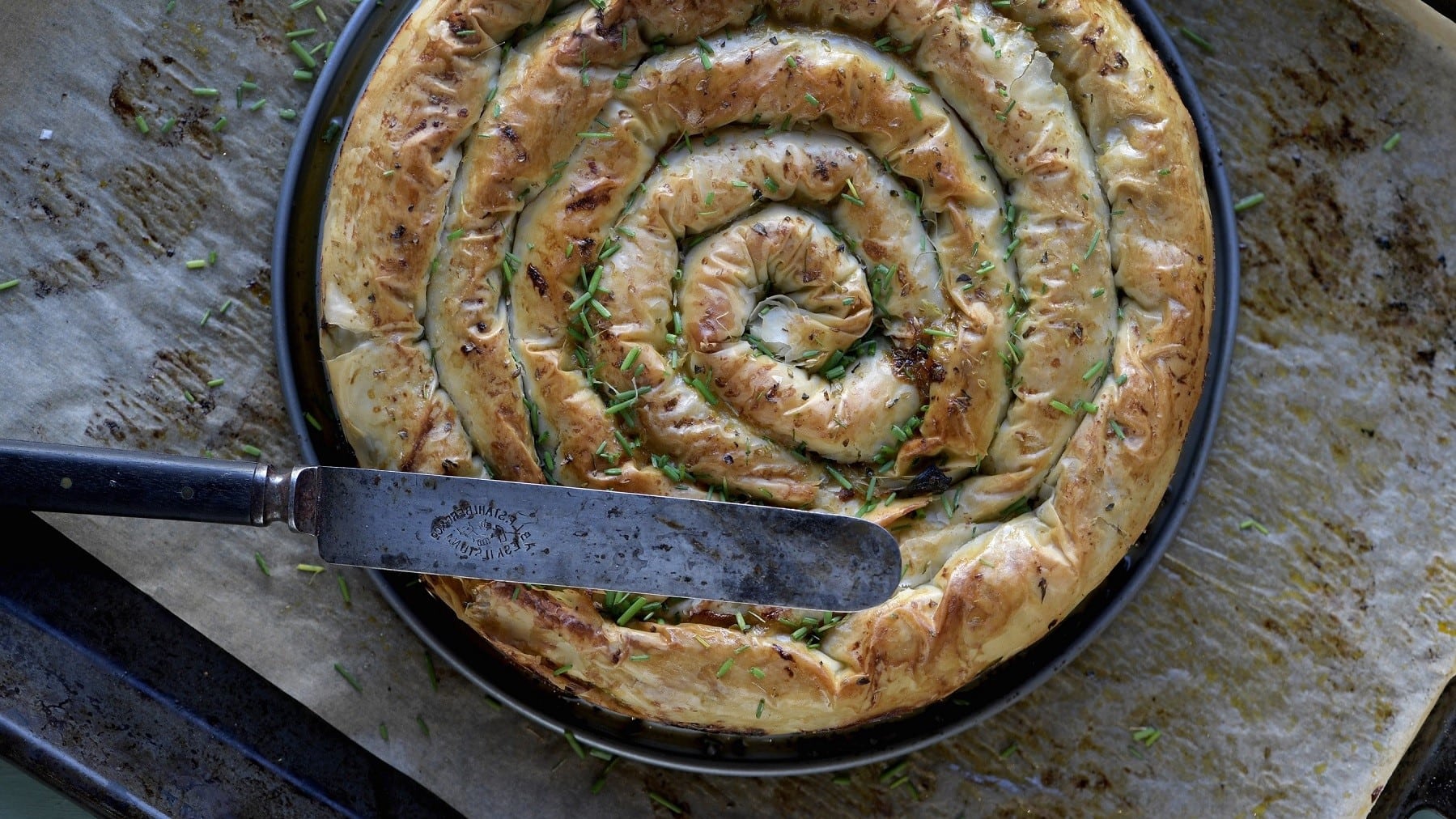 Börek mit Kürbis, Spinat und Feta, zu einer Schnecke aufgerollt serviert in einer gusseisernen Pfanne und garniert mit frischem Schnittlauch.