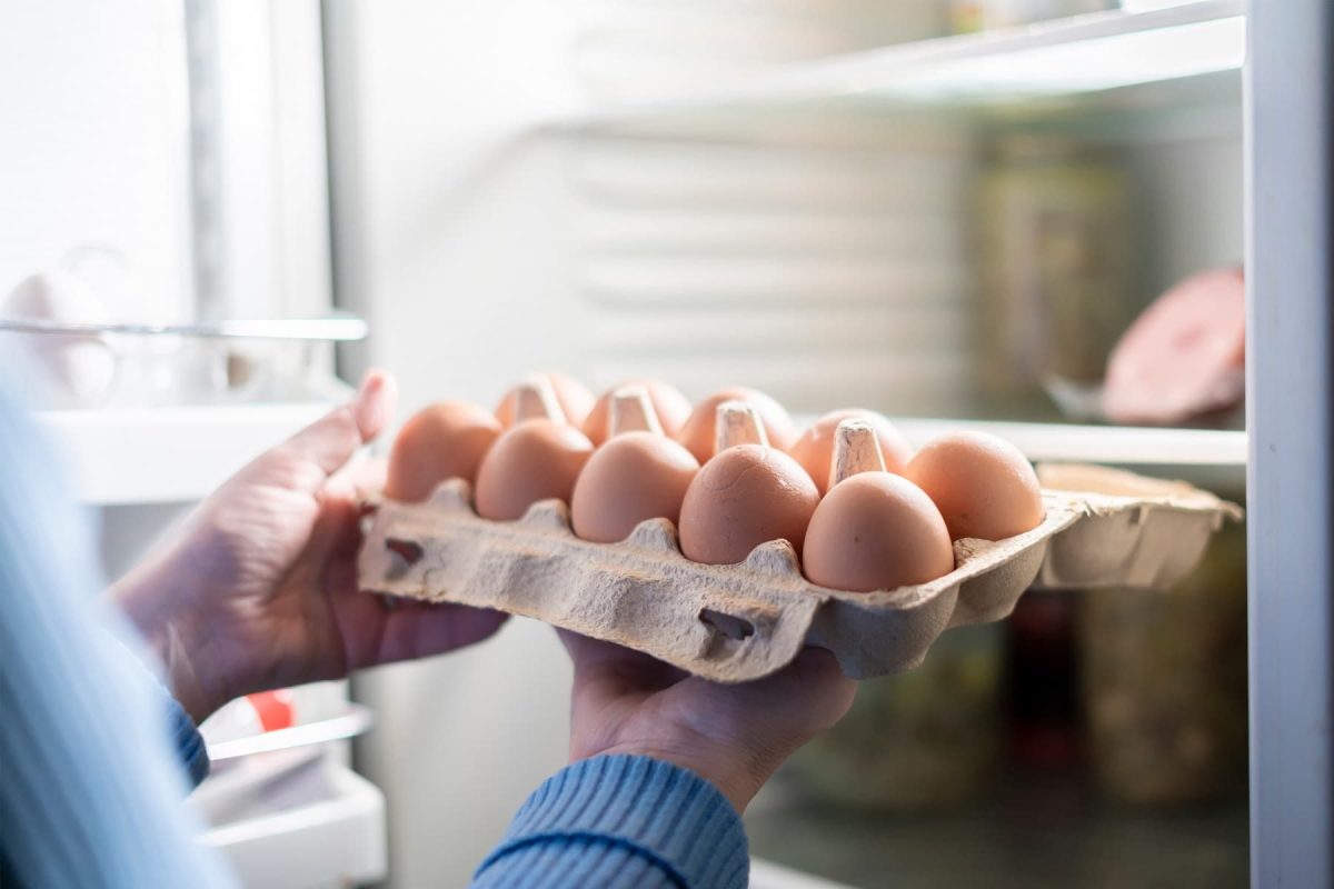 Eine Frau holt eine Packung Eier aus dem Kühlschrank.