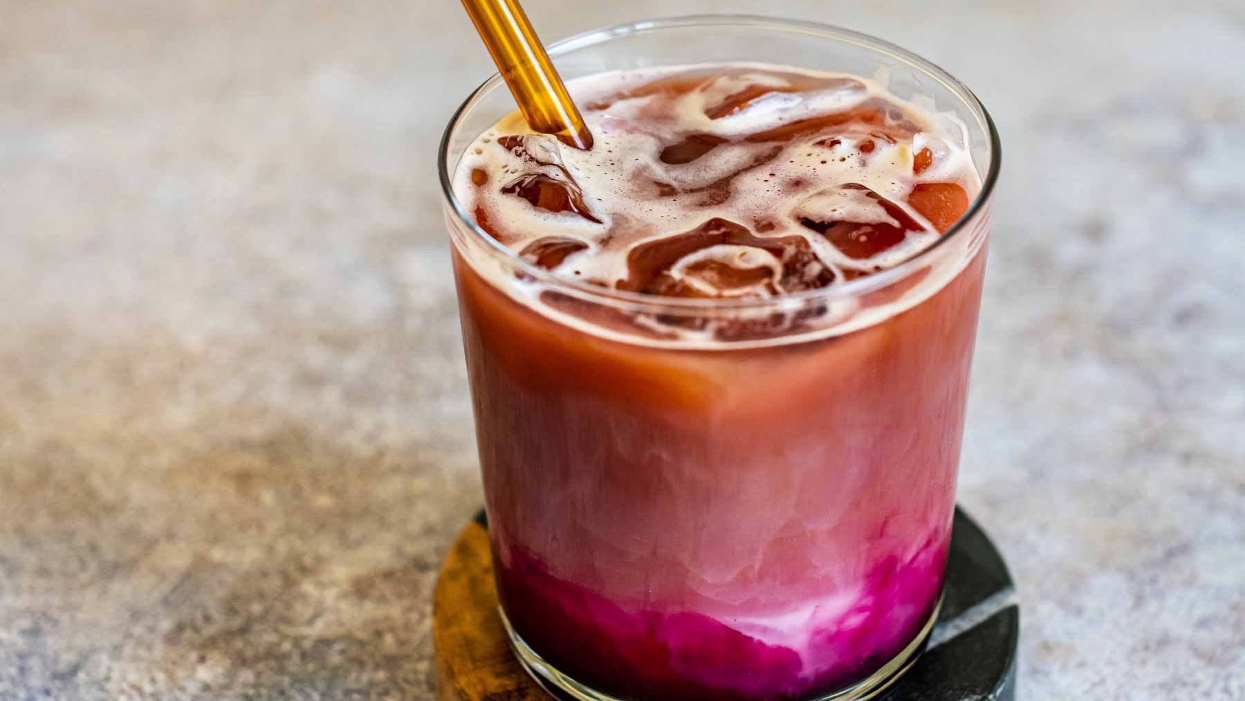 Rote-Bete-Latte mit Eiswürfeln in einem Drink-Glas auf Marmortisch.