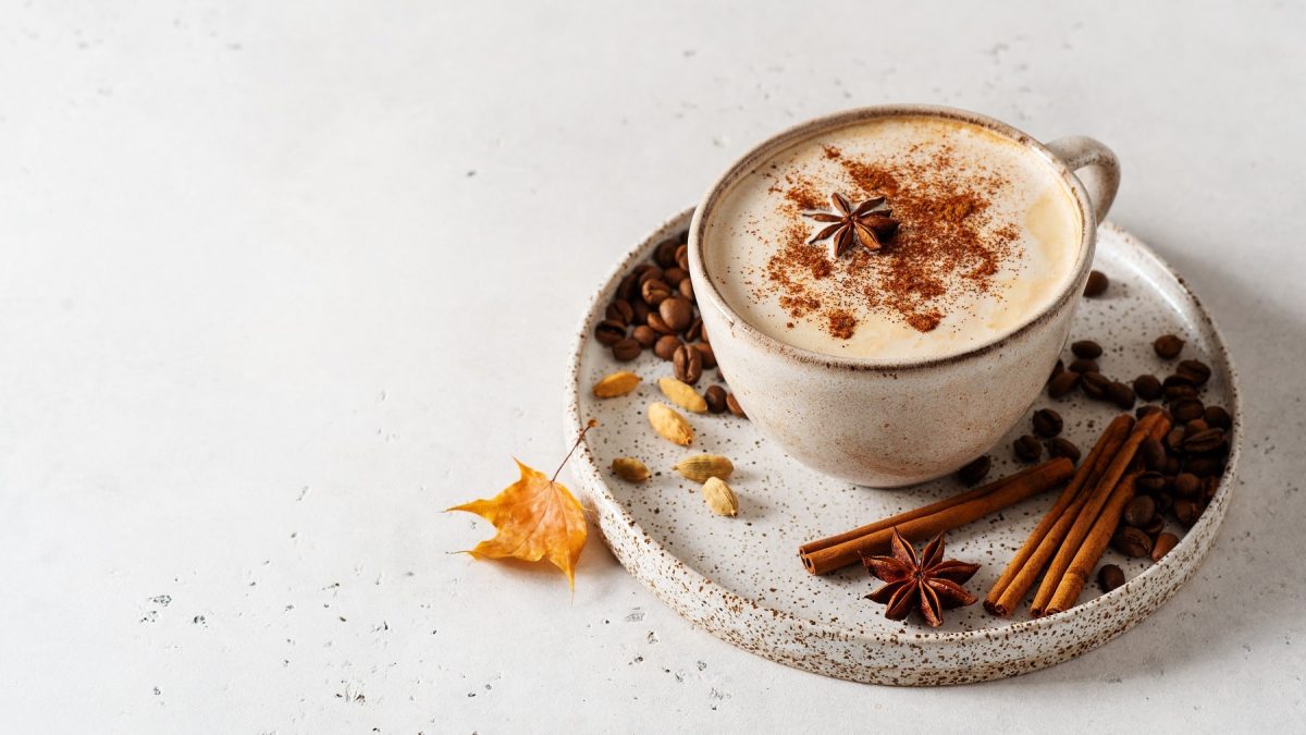 Eine Tasse Chai Vanilla Coffee mit Anis und Muskat dekoriert, auf der Untertasse lieben Gewürze wie Zimtstangen und Kardamom.