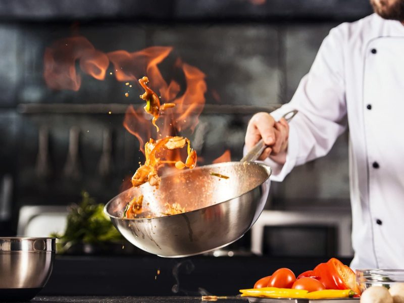 eat! Berlin 2022: Ein Koch schwenkt einen Wok, aus dem eine Flamme aufsteigt.