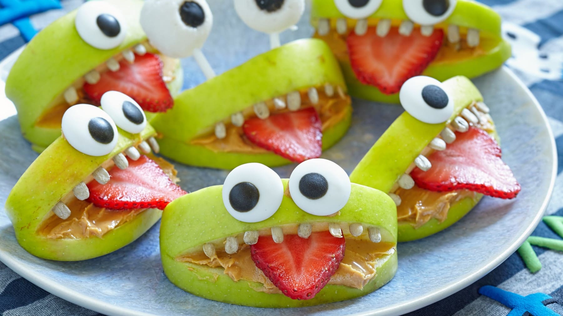 Mehrere gesunde Apfel-Monsterchen auf einem Teller vor blauem Hintergrund.