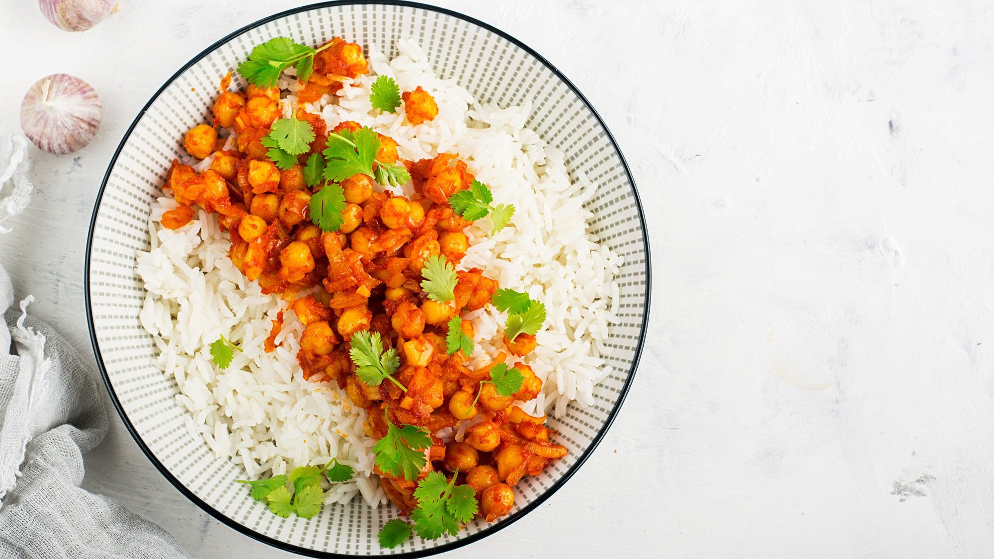 Ein Teller Kichererbsen-Erdnuss-Curry mit Reis und Koriander in der Draufsicht.