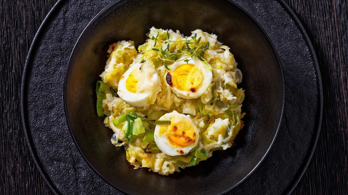 Anglesey Eggs – überbackene Eier auf Kartoffelpüree in Käsesauce auf schwarzem Teller.