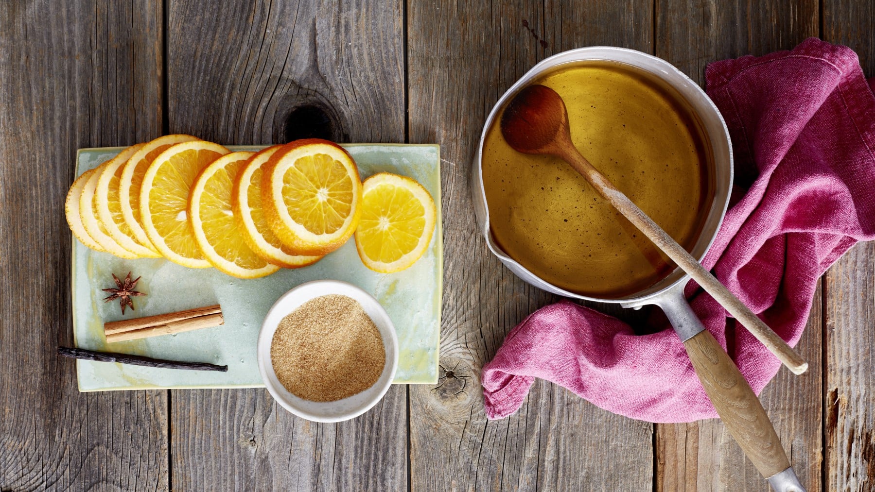 Bratapfelpunsch, im Topf serviert, dazu frische Oraangenscheiben und eine Schale Zimt und Zucker.