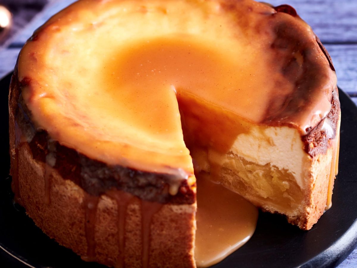 Auf einem Teller steht ein Käsekuchen mit Apfelkompott und Lebkuchenkaramell. Er ist angeschnitten und man erkennt die Füllung.