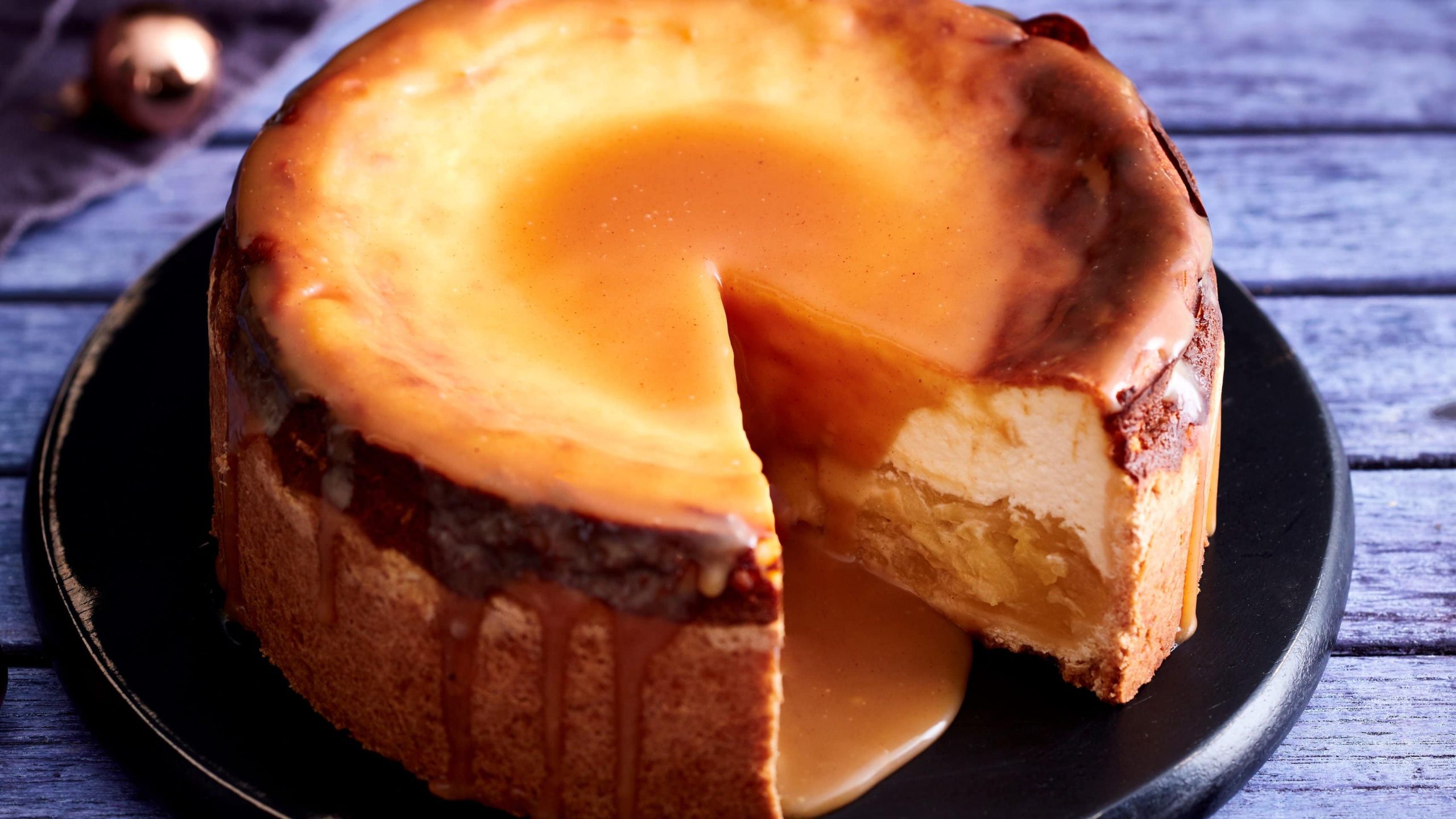 Auf einem Teller steht ein Käsekuchen mit Apfelkompott und Lebkuchenkaramell. Er ist angeschnitten und man erkennt die Füllung.