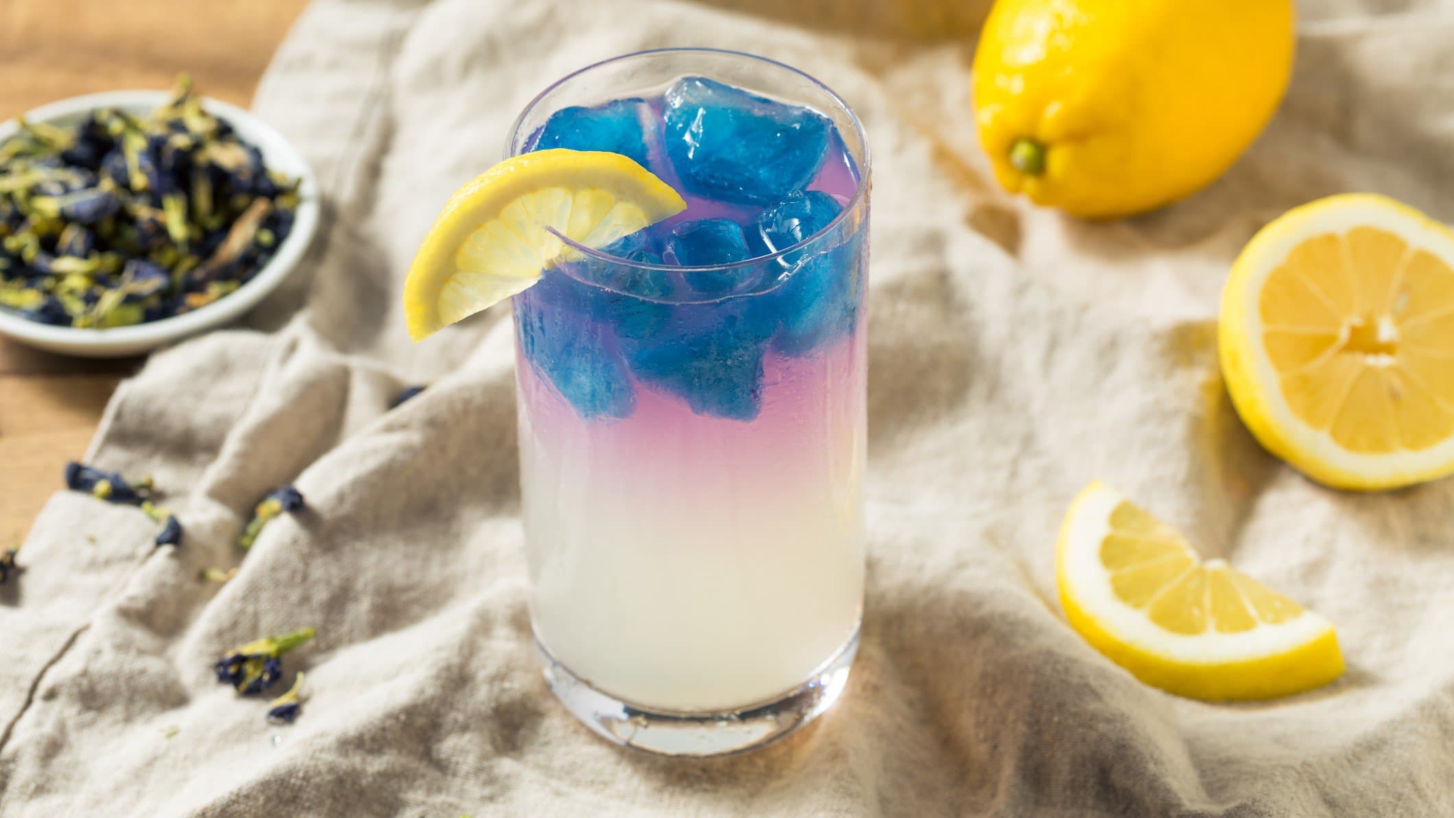 Ein Glas mit der gelben Zitronenmarmelade udn blauen Eiswürfeln.