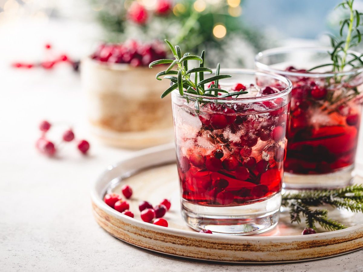 Zwei Gläser Cranberry Paloma in weihnachtlichem Setting mit Lichertektten und etwas Tannengrün im Hintergrund.
