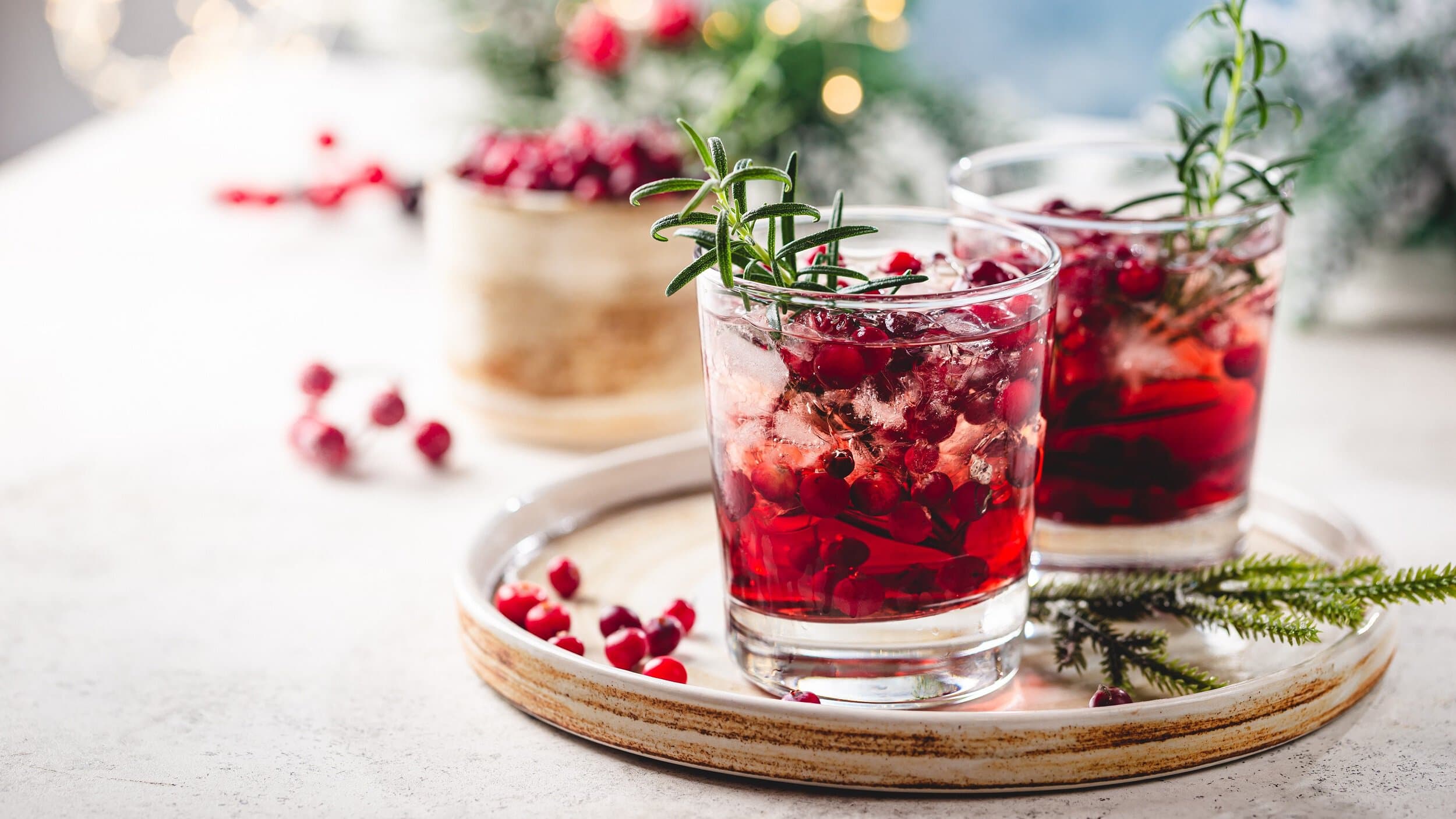 Zwei Gläser Cranberry Paloma in weihnachtlichem Setting mit Lichertektten und etwas Tannengrün im Hintergrund.
