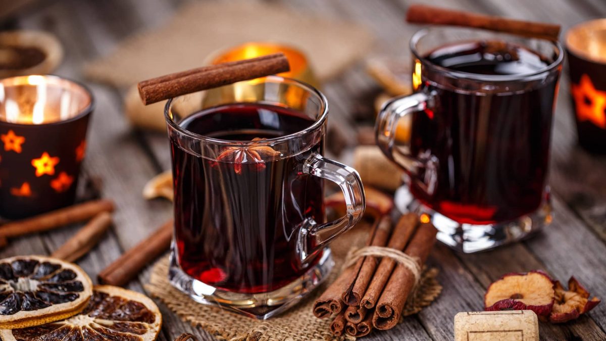 Zwei Gläser mit Glühwein mit Rum und Tee, drumherum liegen viele Gewürze wie Zimtstangen, Anis und getrocknetes Obst.