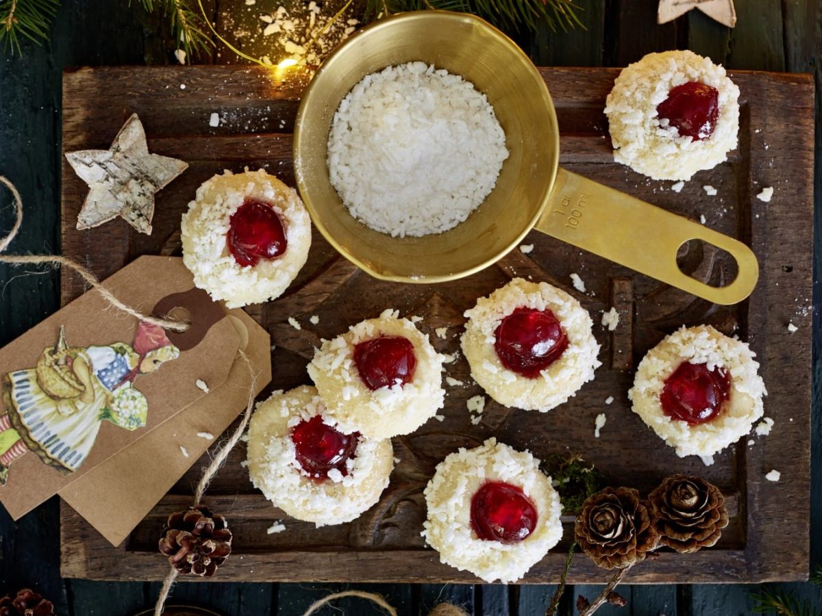 Rotkäppchen-Kekse mit Kokosraspeln und Puderzucker verziert, serviert auf einem Holzbrett mit allerlei weihnachtlicher Dekoration.