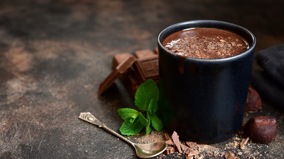 Ein Becher After Eight Hot Chocolate, daneben gekrümelte Schokolade, Minze und ein Löffel.