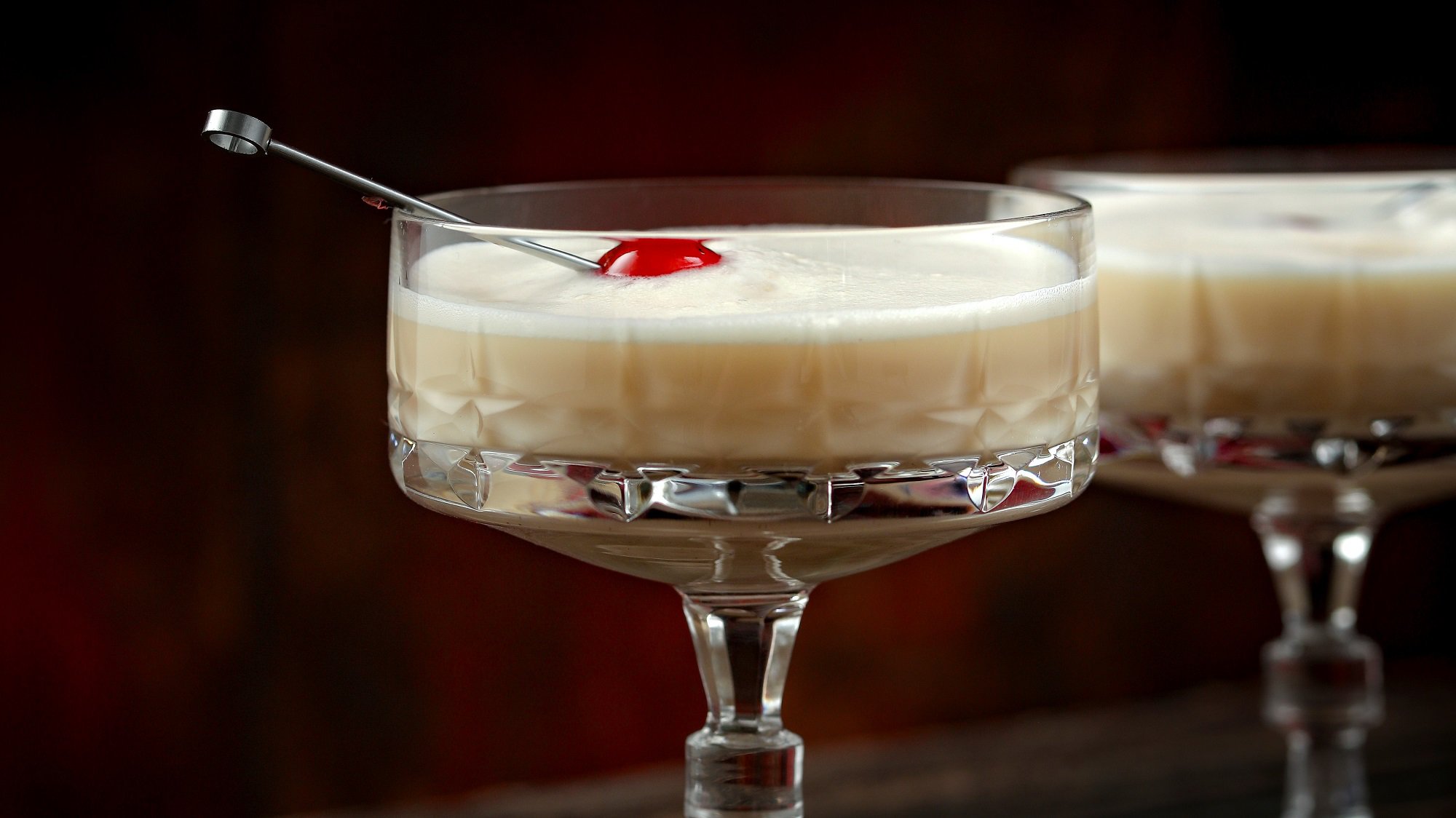 Ein Glas Cherry Flip, ein weißer Cocktail mit einer Cocktail-Kirsche auf einem Spieß.
