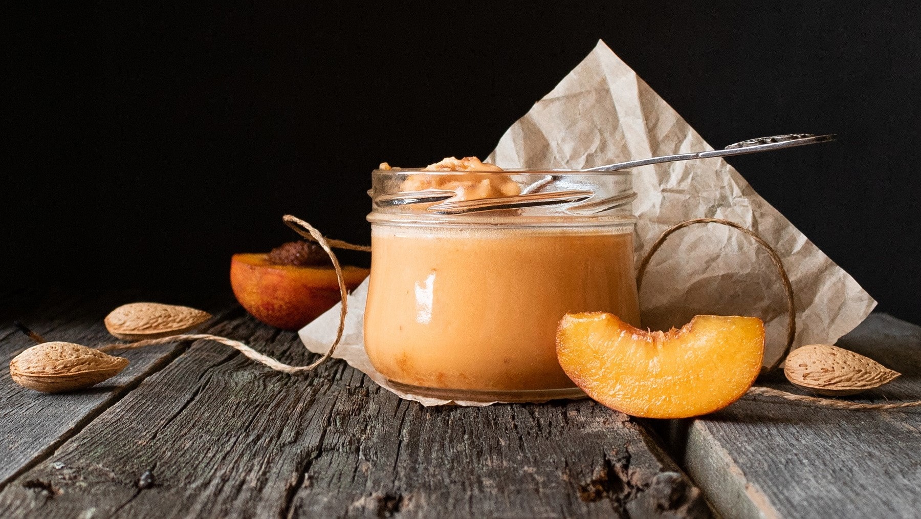 Honig-Creme mit Aprikosen und Mandelmus, serviert in einem kleinen Dessertglas auf einem rustikalen Holztisch.
