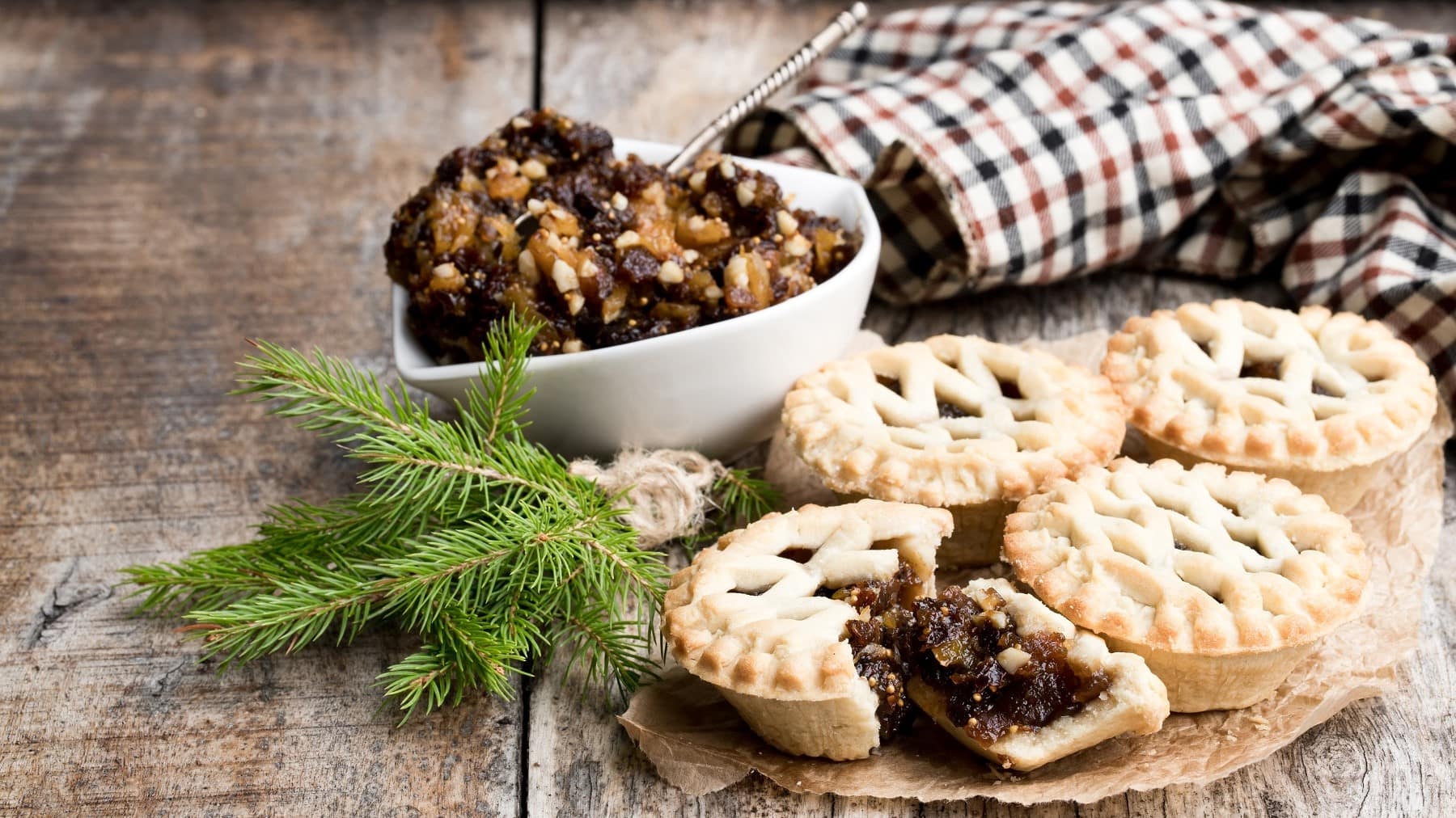 Mincemeat Pies mit frichem Mincemeat, bestäubt mit Puderzucker und angebrochen serviert auf einem hölzernen Tisch mit weihnachtlichem Dekor.