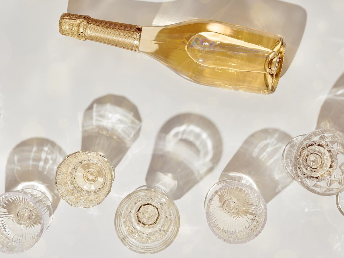 Prosecco im Kühlschrank: mehrere gefüllte Sektgläser in der Draufsicht, die von der Sonne bestrahlt einen Schatten werfen, daneben liegt eine Sektflasche.