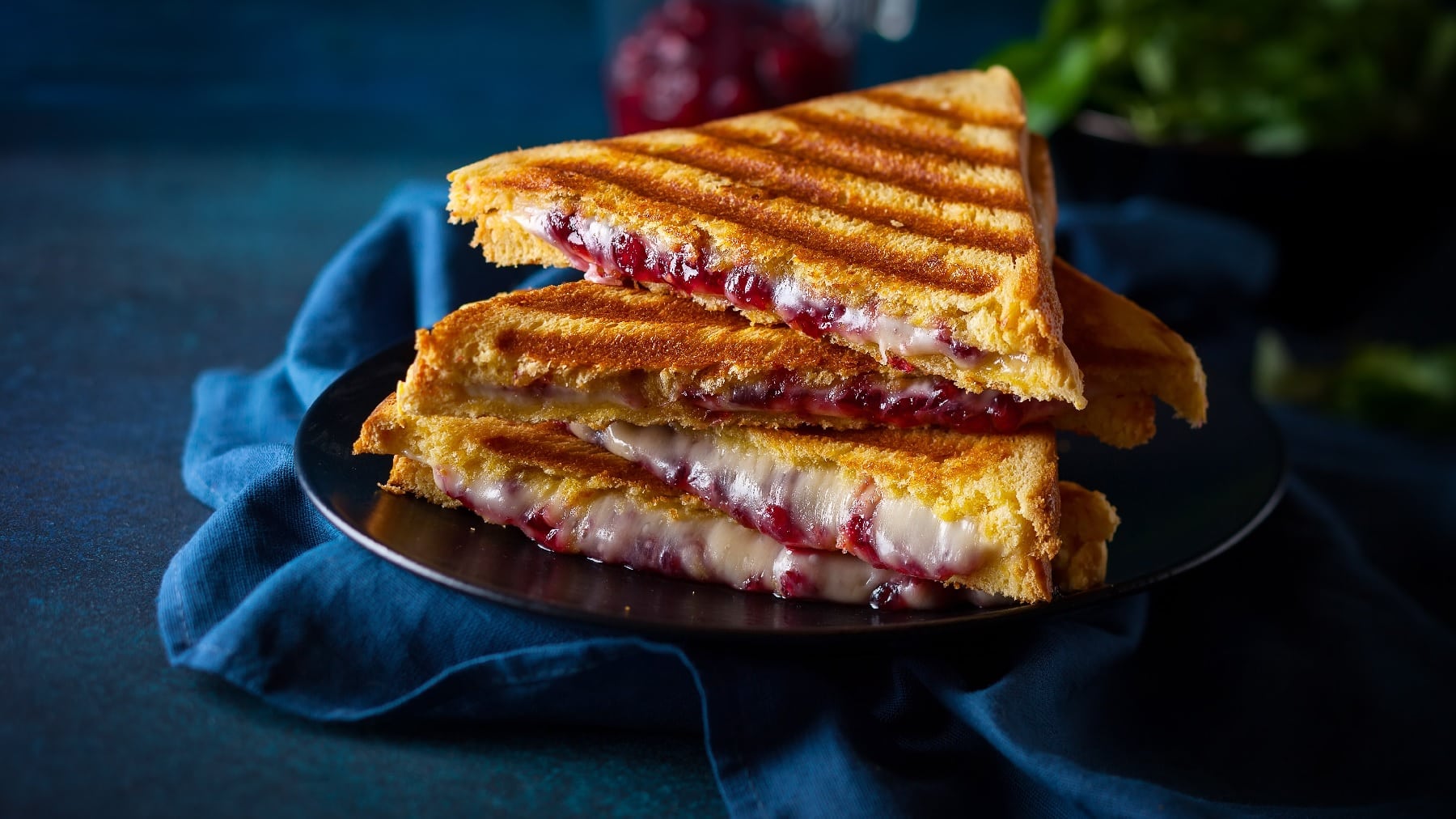 Halbierte Toastscheiben mit dem Käse und Cranberry-Senf auf dunkelblauem Untergrund.