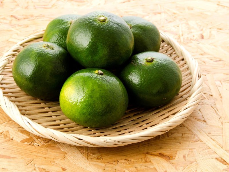 Was sind grüne Mandarinen? Satsumas in einem Bastkorb auf Holztisch. Draufsicht.