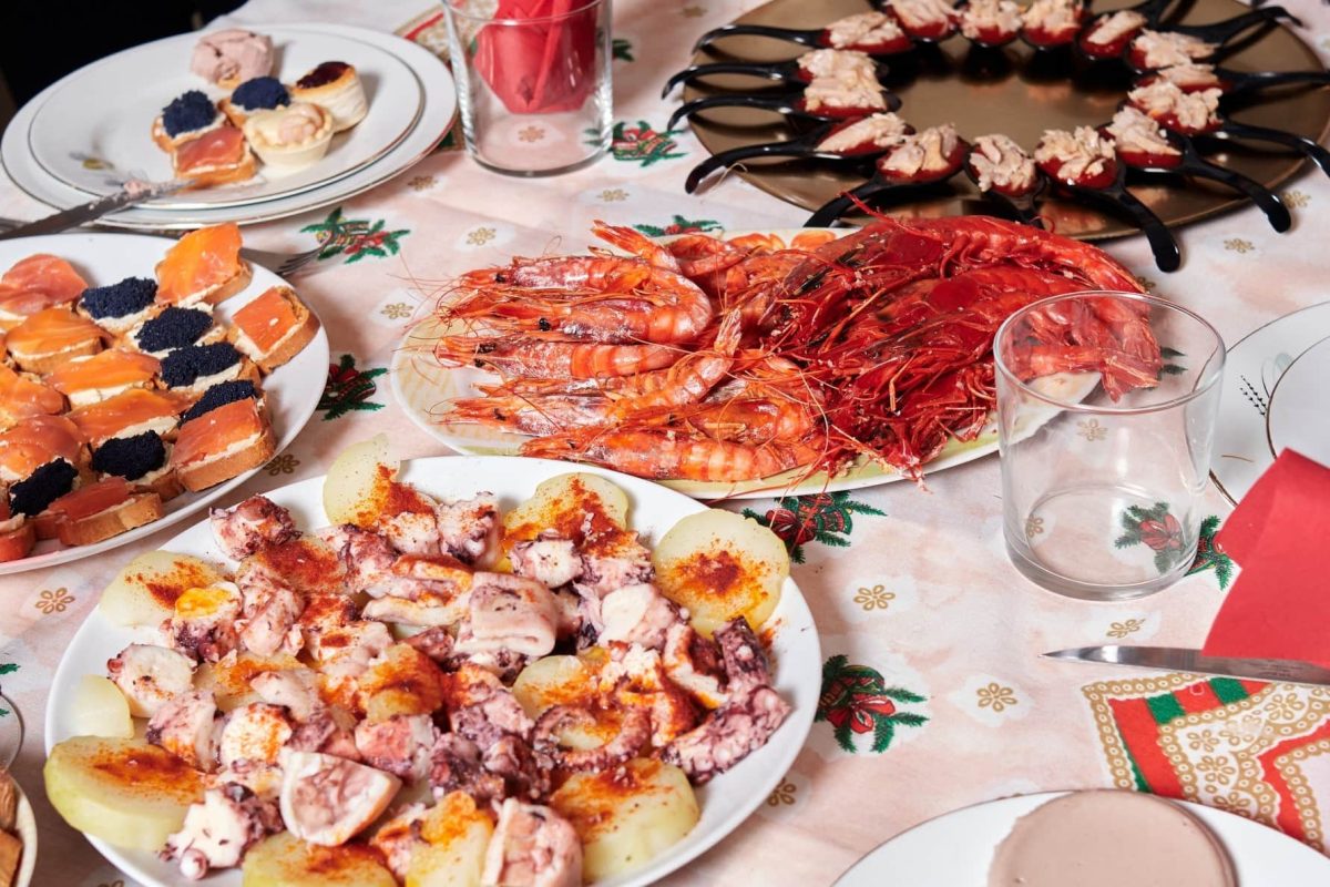 Spanisches Weihnachtsessen aus diversen Speisen auf Tellern und Häppchen auf gedecktem Tisch. Draufsicht.