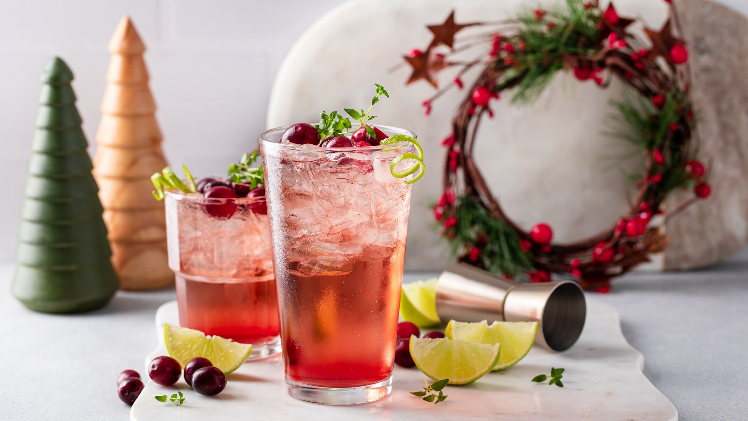 Zwei Gläser Tipsy Rudolph, ein roter Cocktail mit Wodka, darin Oregano, Cranberrys und Eiswürfel. Drumherum Weihnachtsdeko.
