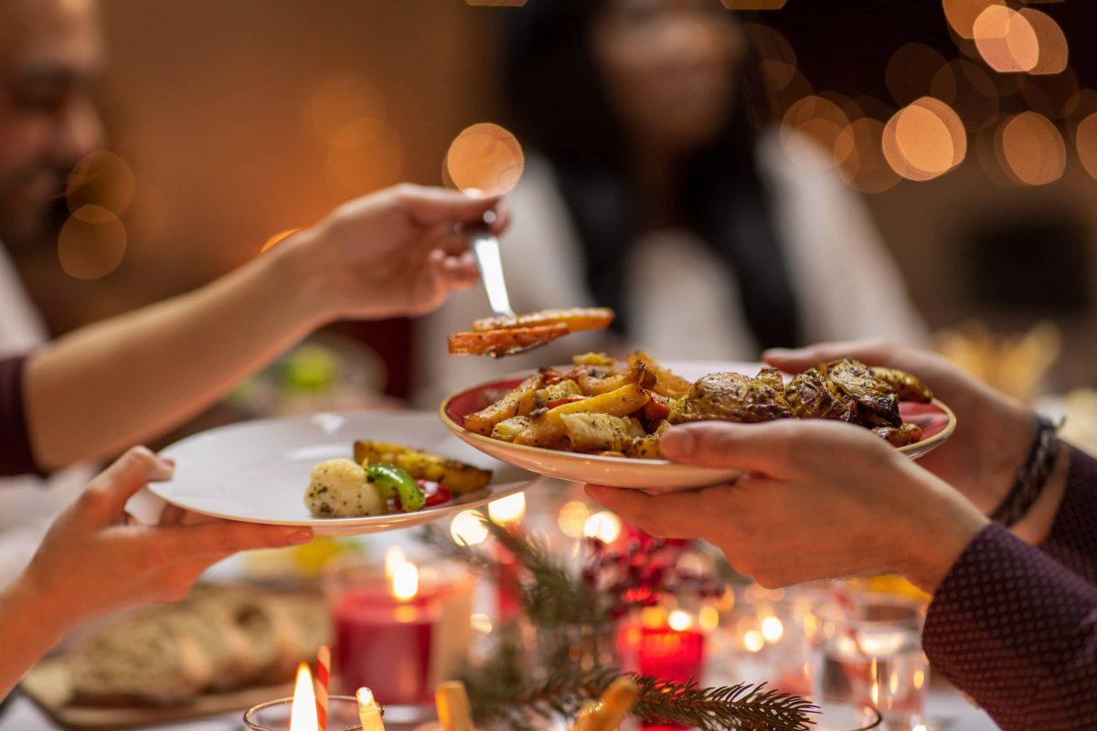 veganes Weihnachtsdinner: eine Frau füllt einem Gast Essen auf einen Teller.