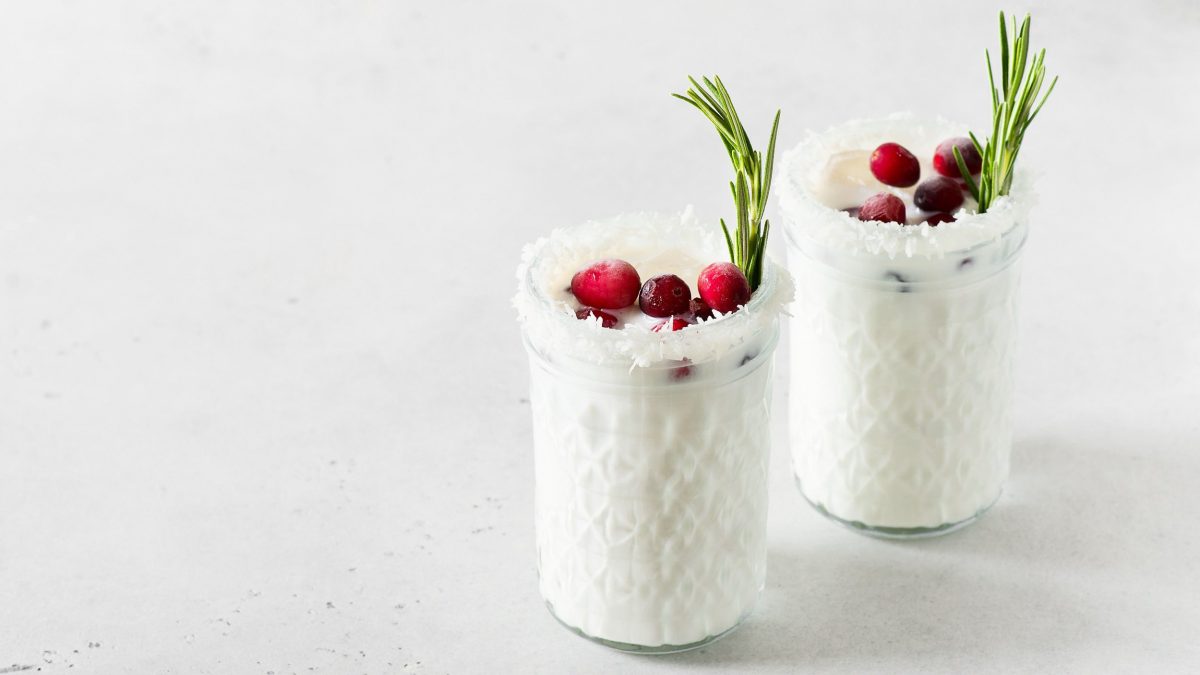 Zwei Gläser White Christmas Margarita mit Kokosraspeln, Rosmarin und Cranberrys garniert.