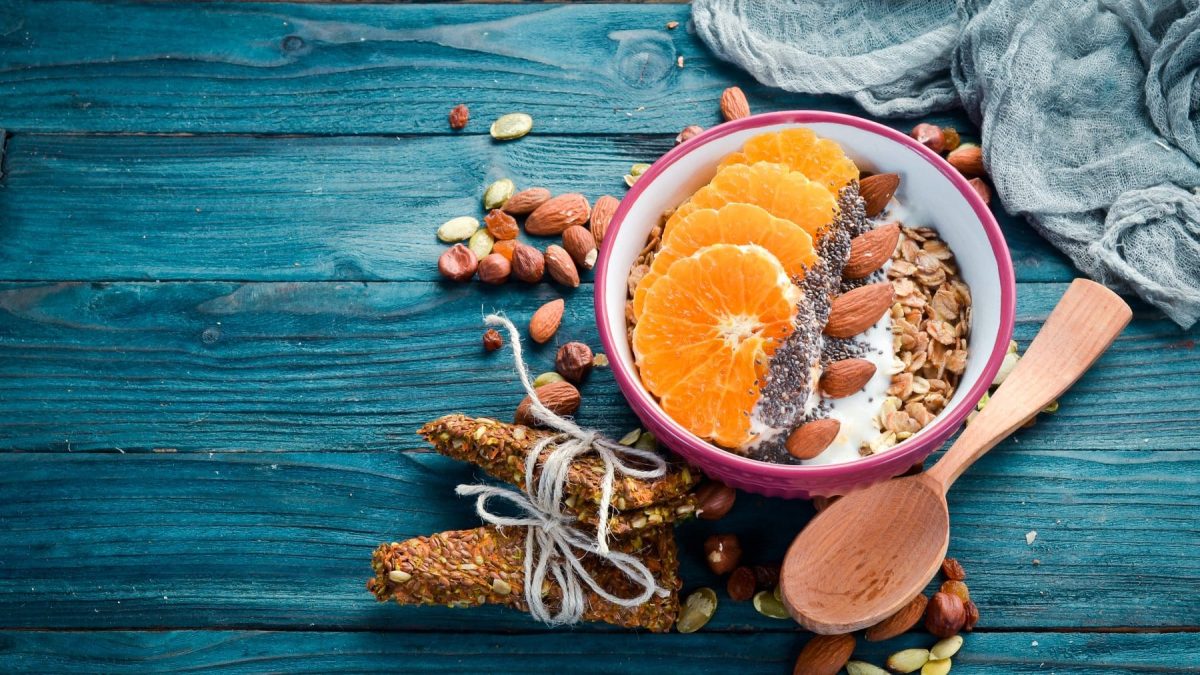 Vegane Superfood-Frühstücksbowl mit Mandarinen und Maracuja mit den Zutaten und Holzlöffel auf blauem Untergrund. Draufsicht.