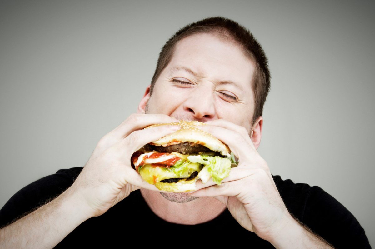 Burger essen ohne Kleckern japanische Methode mit dem Japan-Griff isst ein Mann einen Burger mit beiden Händen. Frontalansicht.
