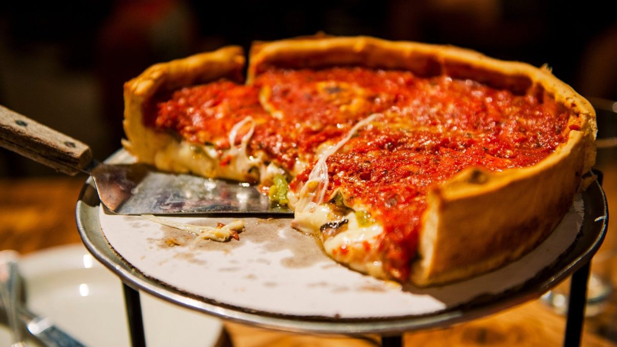 Eine angeschnittene Chicago Deep Dish Pizza mit Käse gefüllt und Tomatensauce bedeckt, auf einem Pizzaständer.