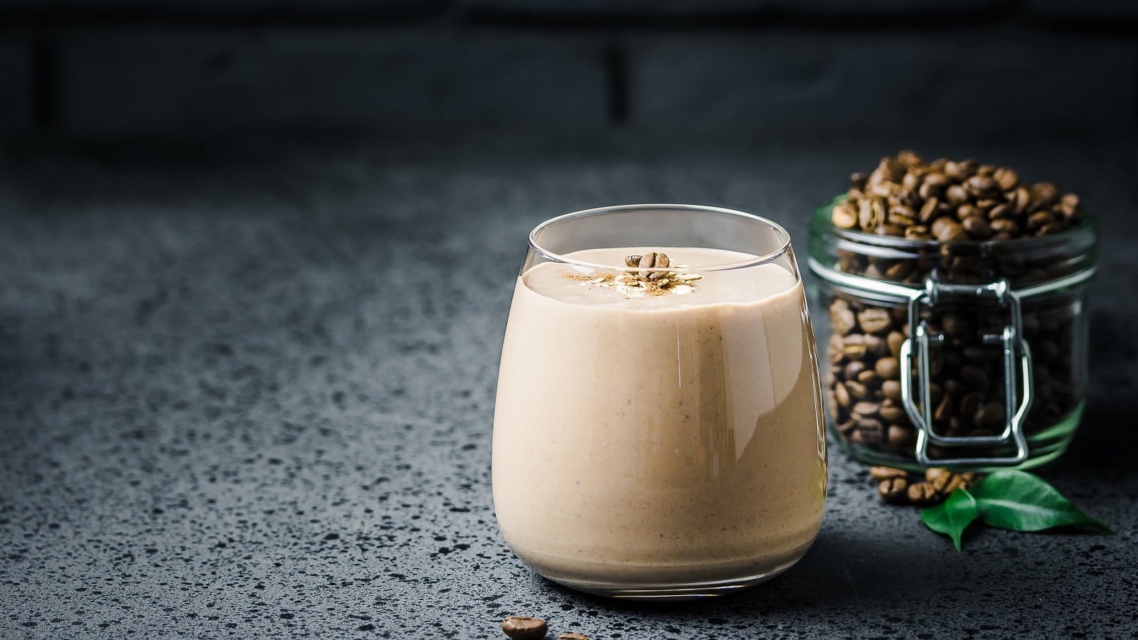 Ein Glas mit Peanut Butter Latte neben einem Glas mit Kaffeebohnen.