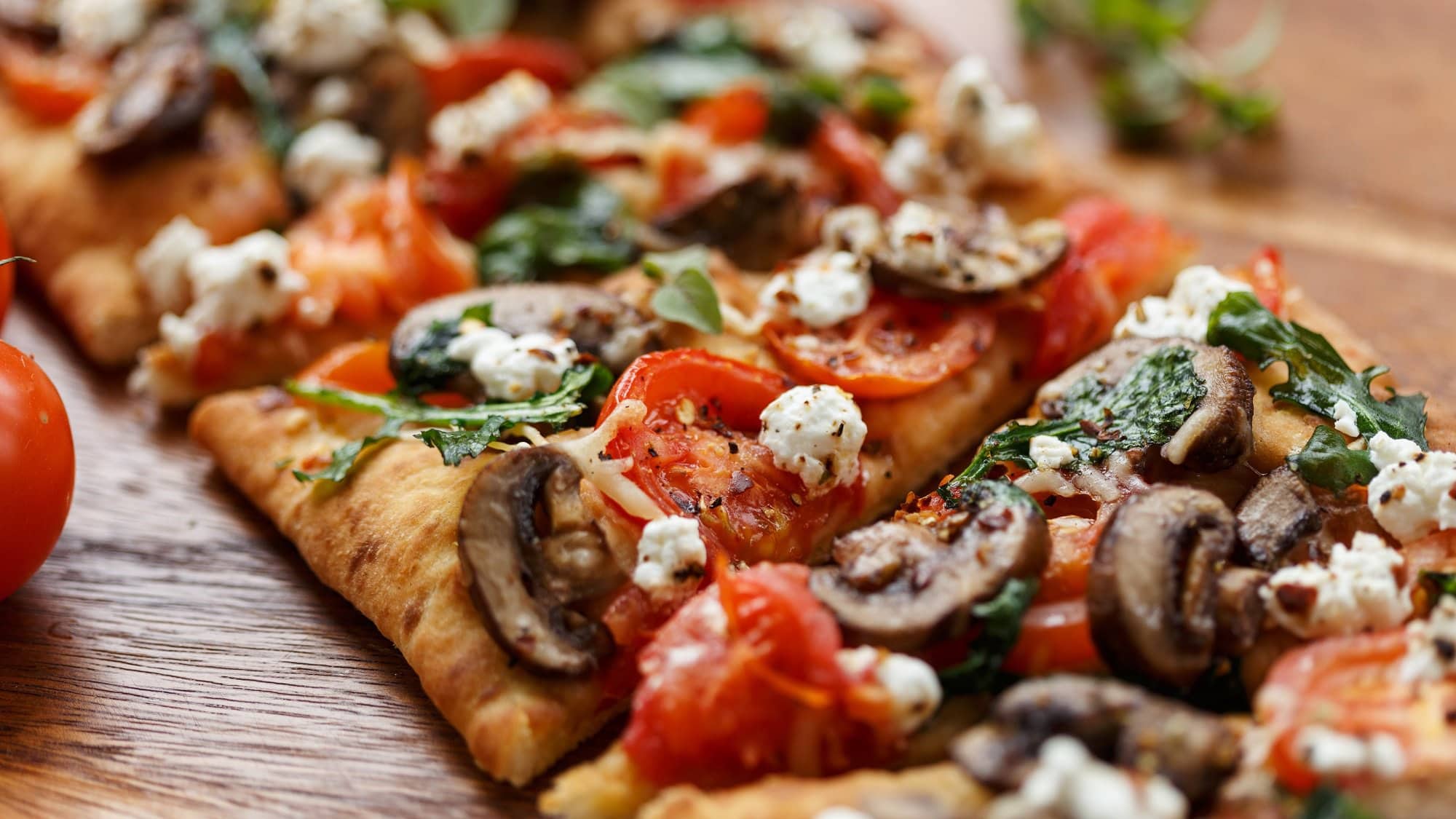 Eine in Stücke geschnittene Flatbread Pizza mit Pilzen, Tomaten, Rucola und Fetakäse.