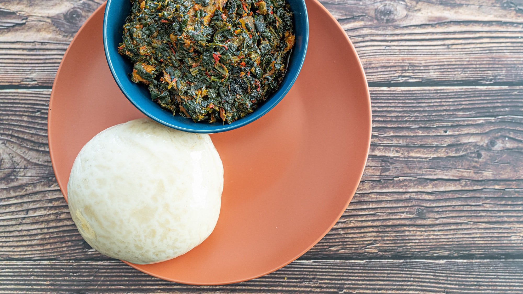 Fufu, ein afrikanischer Kloß, auf einem Teller mit einer Schüssel eines afrikanischen Gemüseeintopfes, Draufsicht.