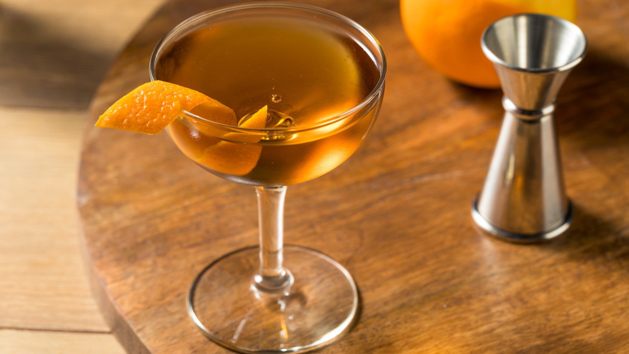 Hanky Panky Cocktail in Cocktailschale mit Orangenzeste auf Holztisch. Daneben Barmaß und eine Orange. Draufsicht.