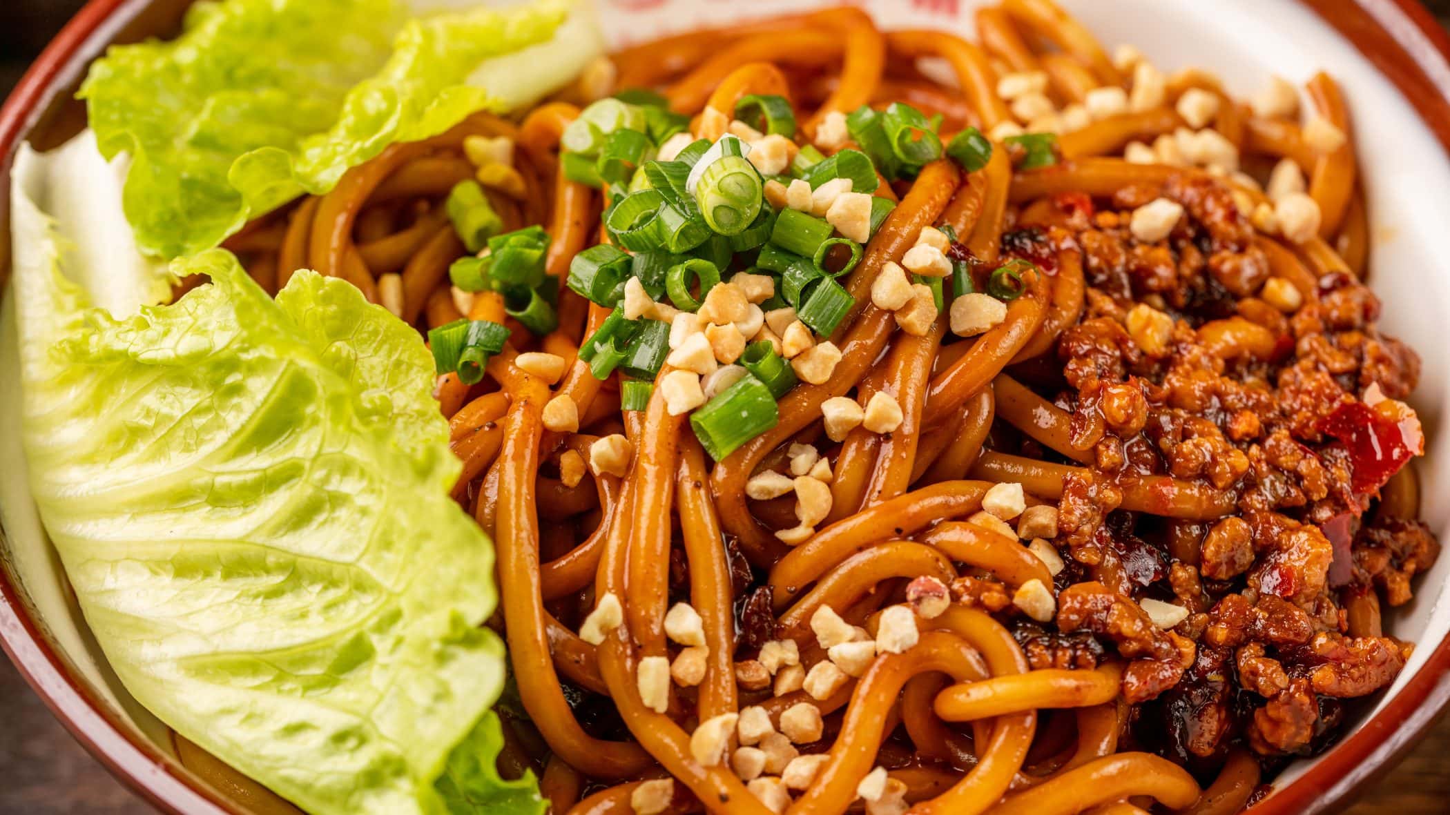 Chinese Hot and Dry Noodles mit Salatblatt in einer braunen Schale. Draufsicht.