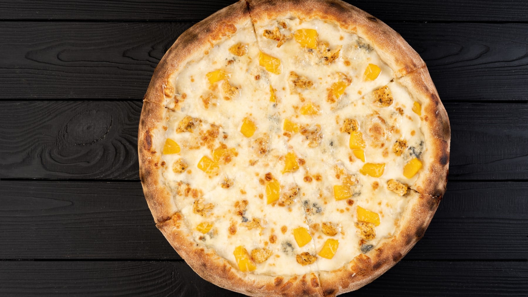 Pizza bianca mit Pfirsich und Gorgonzola vor dunklem Holzhintergrund in der Draufsicht.