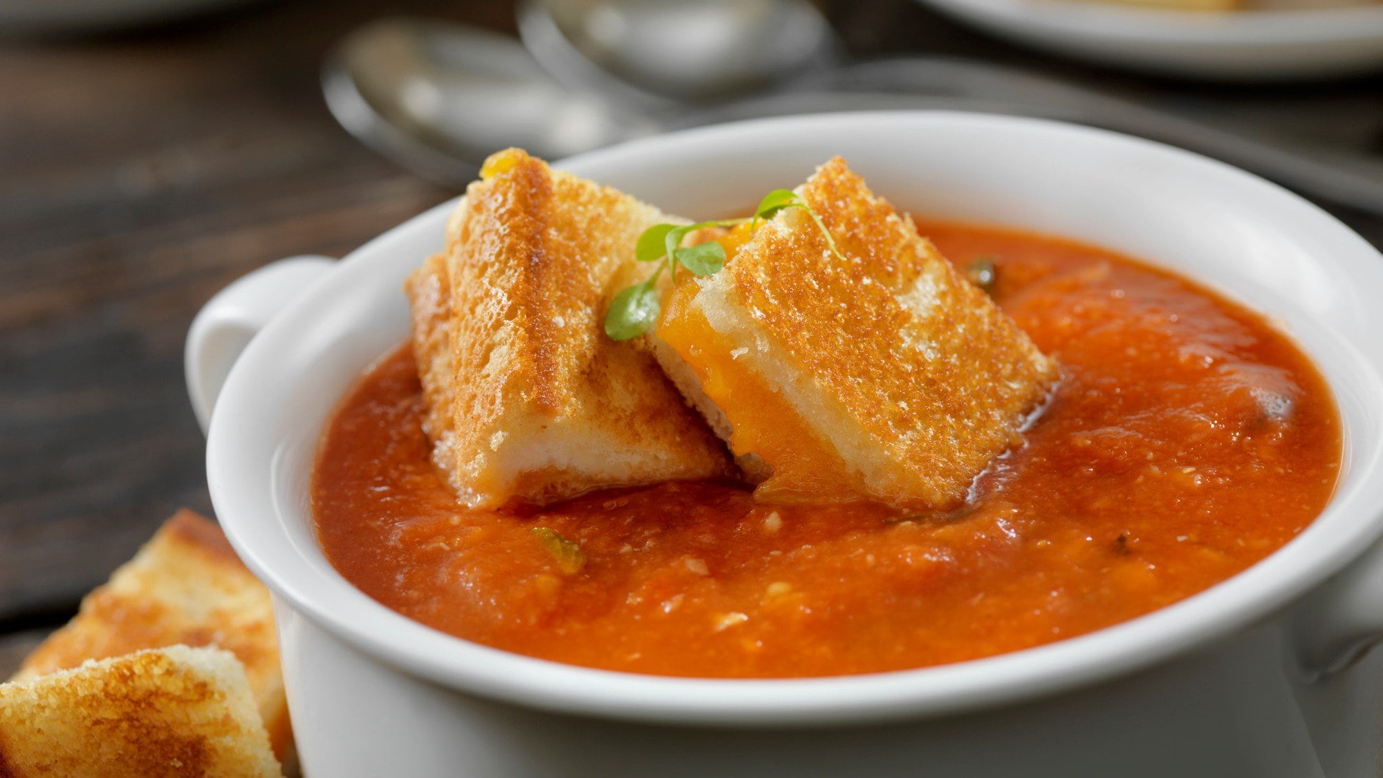 Tomaten-Paprika-Suppe mit Grilled Cheese Croutons in weißer Suppenschüssel. Draufsicht.