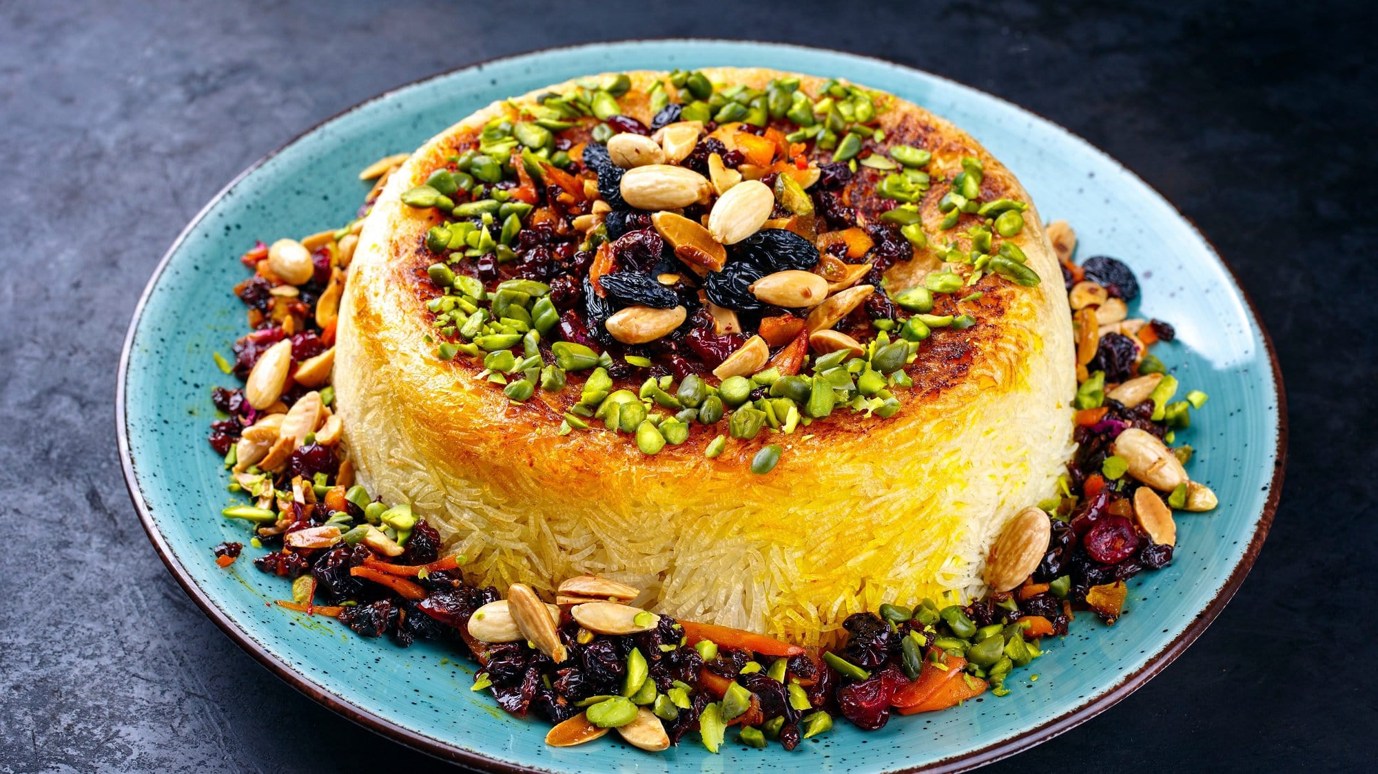 Ein Teller mit Tahdig, persischer Safranreis mit Kruse, darüber viele Nüsse und Trockenfrüchte gestreut.