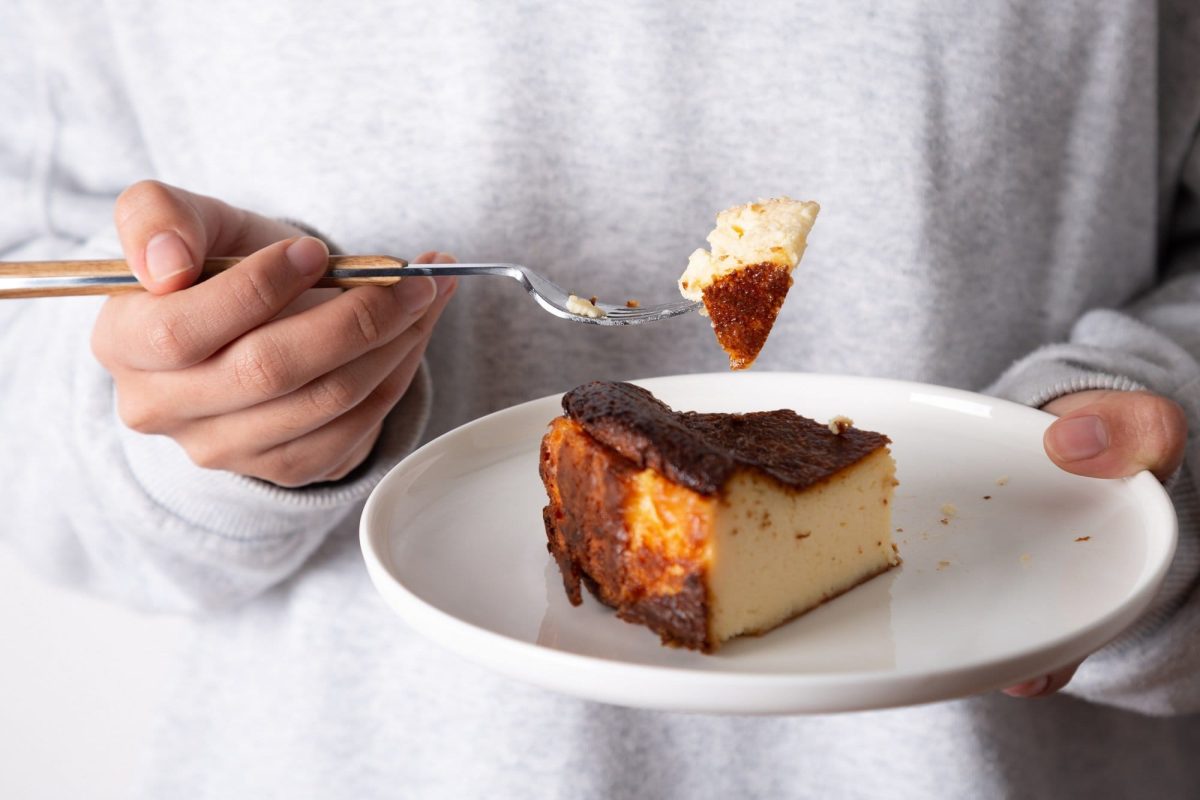 Unterschied zwischen Cheesecake und Käsekuchen: Eine Frau hält einen Teller mit Käsekuchen in der Hand, in der anderen eine Gabel mit einem Stück Kuchen.