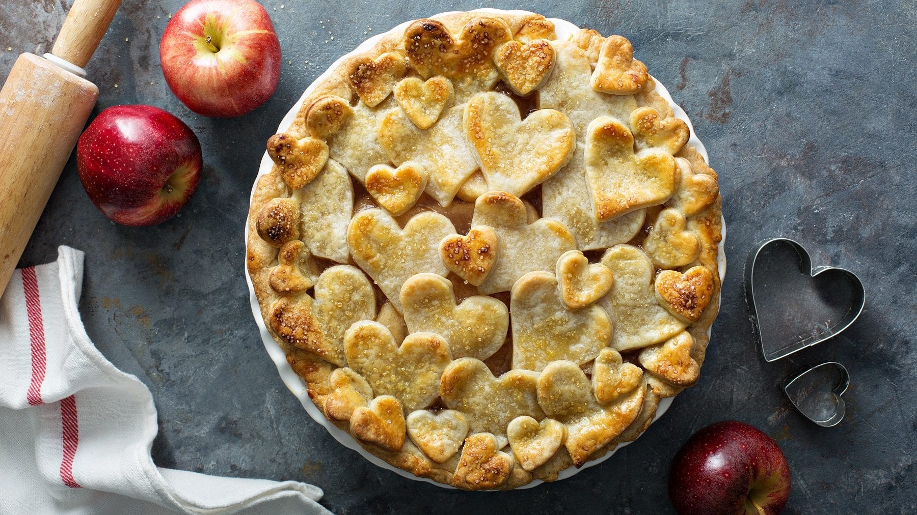 Auf einem Teller ist ein Apfel-Gitterkuchen mit Herzen serviert. Der Teig ist herzförmig gestaltet.