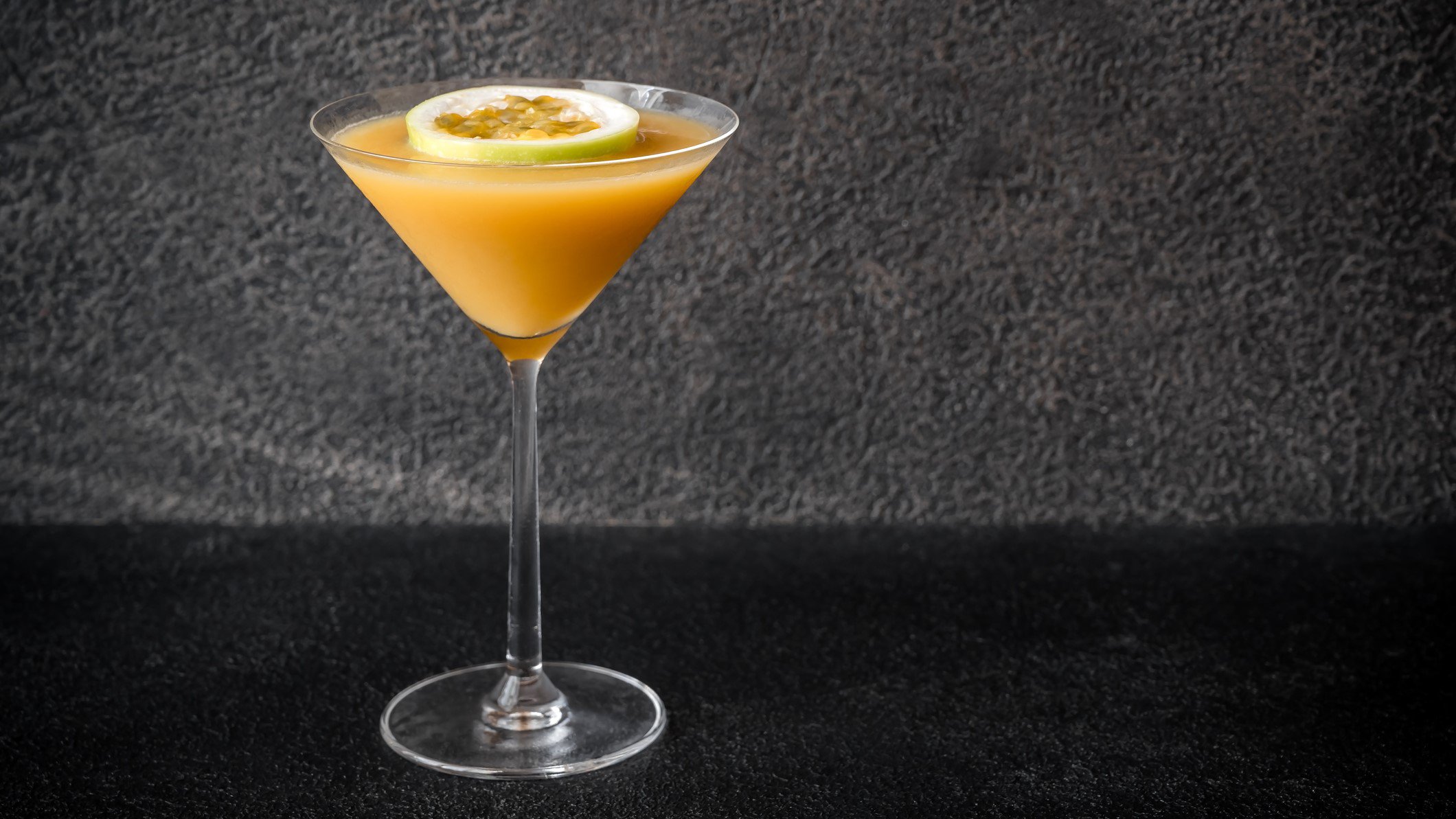 Ein Glas mit Passionfruit Martini auf schwarzem Hintergrund.