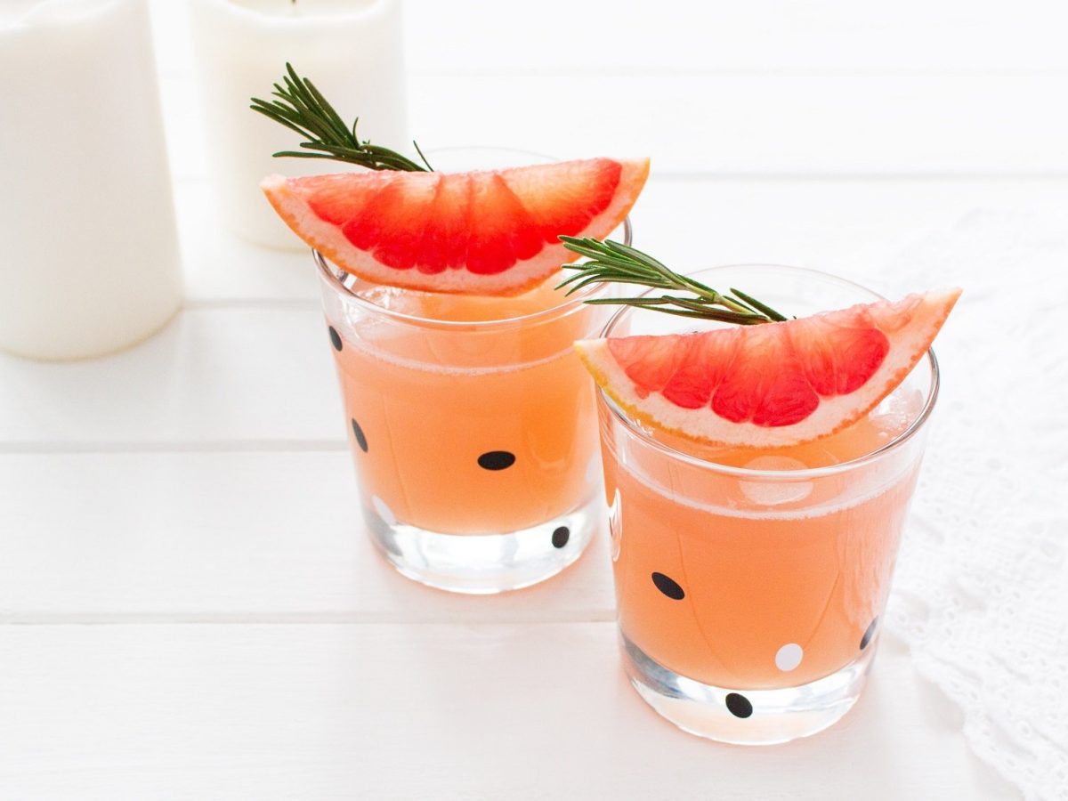 Zwei Shot-Gläser Grapefruit-Sirup mit je einem Zwei Rosmarin und einer Grapefruit-Spalte.