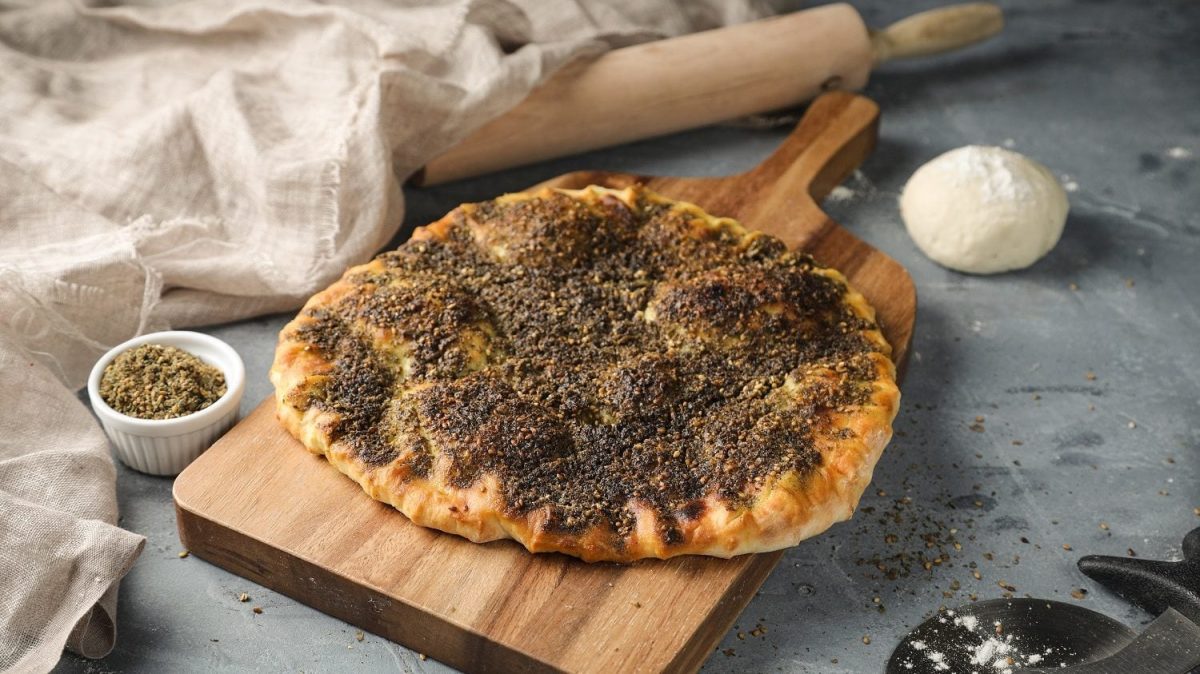 Draufsicht: Auf einem Holzbrettchen liegen eine orientalische Pizza, die auch als Manakish bekannt ist.