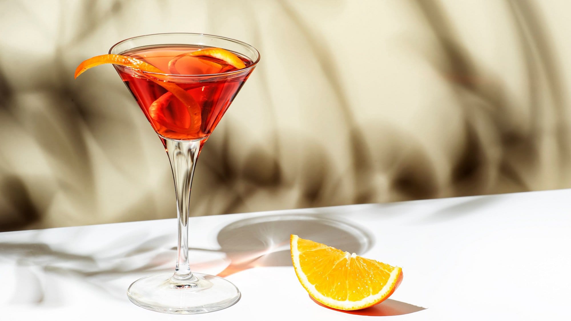 Ein Glas Martinez mit einer Orangenzeste, daneben liegt eine Orangenscheibe